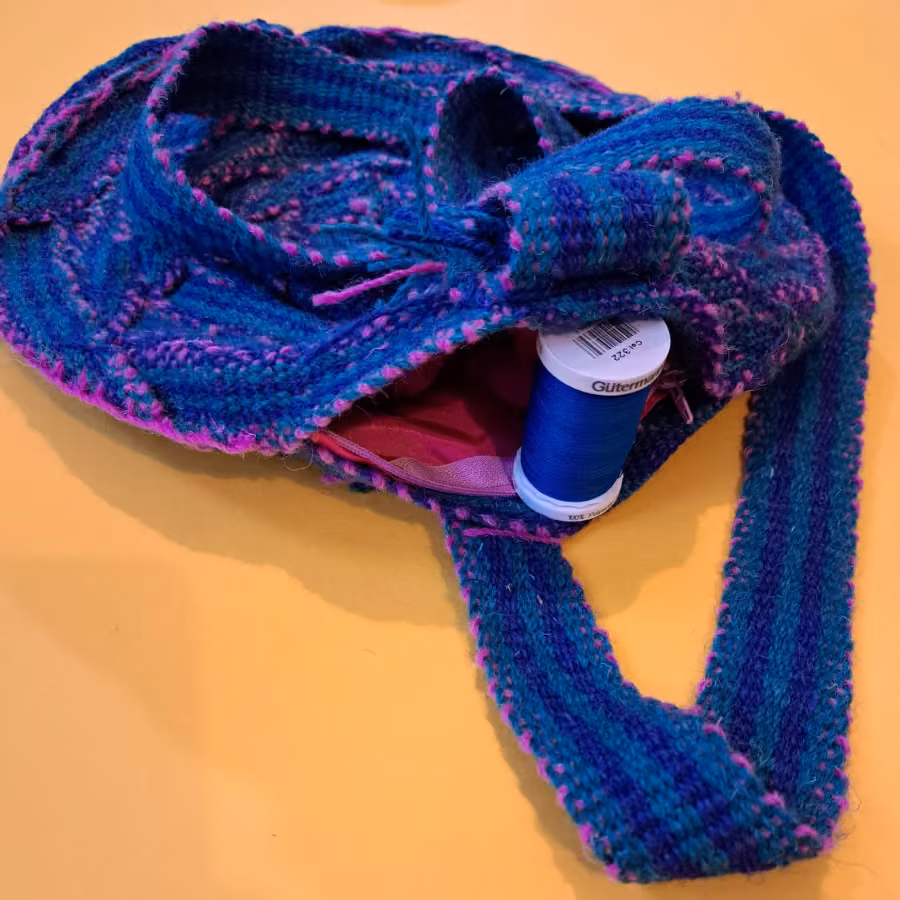 The round inkle bag held open, showing a pink lining and a reel of thread inside