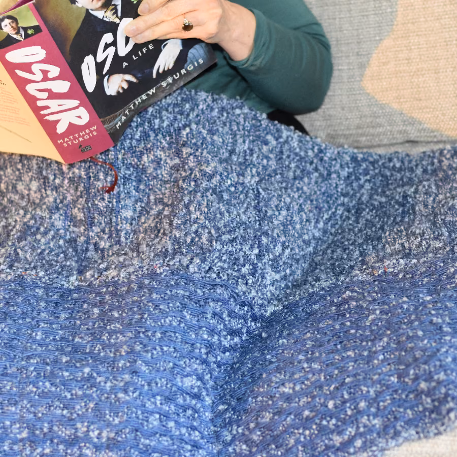 Blue boucle lap wrap spread across someone’s knees as they read a book