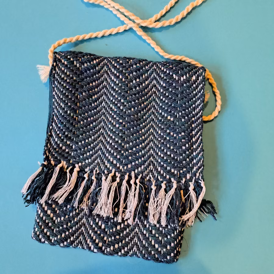 Navy and white herringbone bag with a tasselled fringe along the bottom and a plaited cream strap
