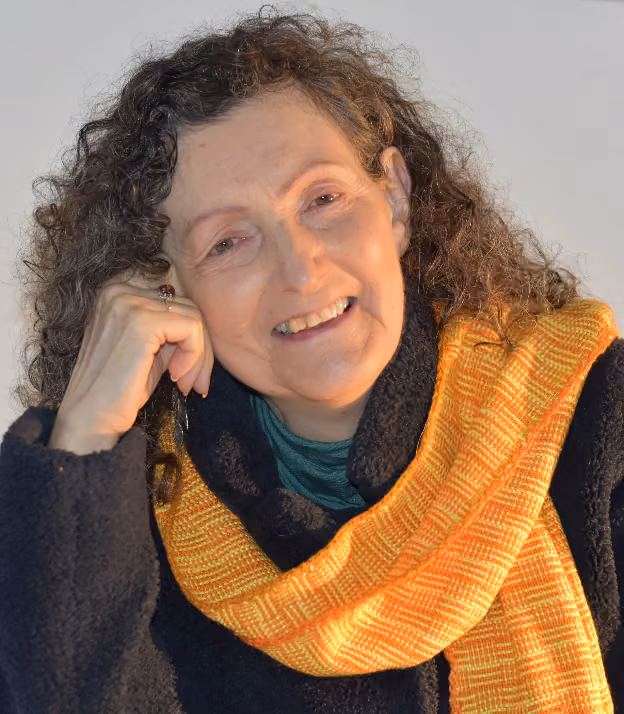 Anne-Marie Wylie smiling, resting her head on her hand, wearing an orange and yellow woven scarf